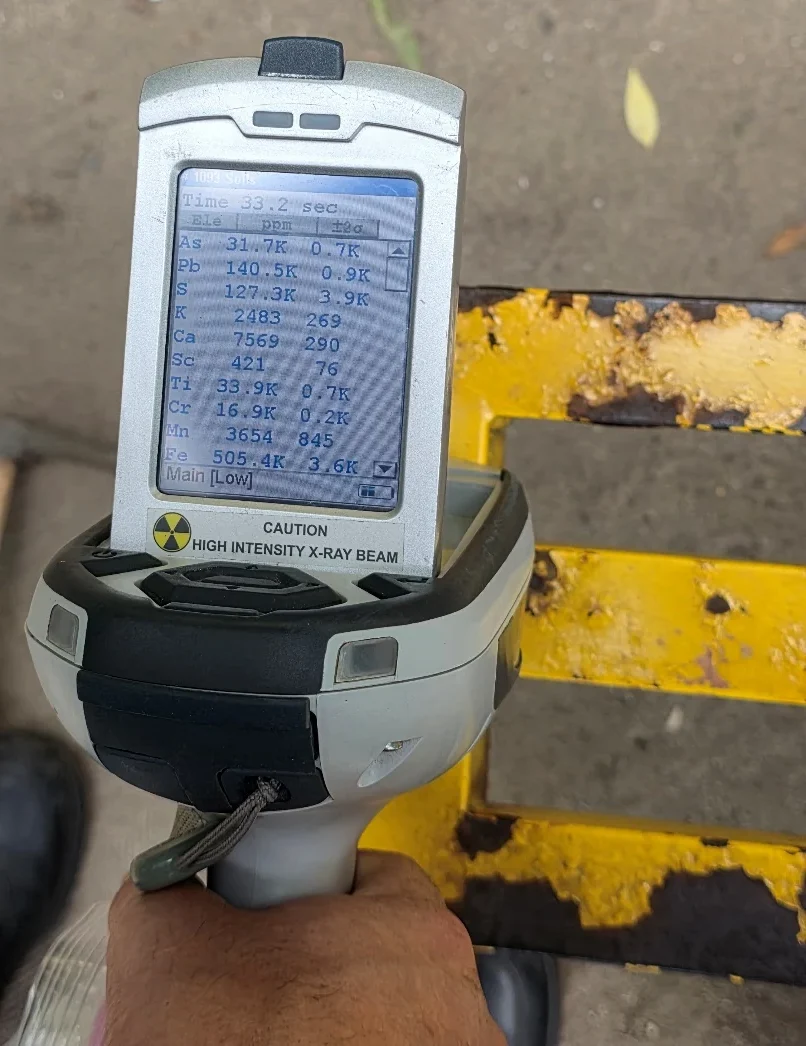 Handheld XRF analyzer testing worn yellow paint on playground equipment in Oskemen.